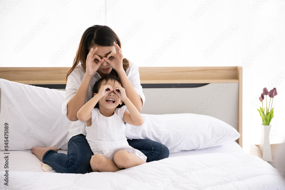 Happy Asian family. Single mother and kid daughter aged three playing together on the bed in the house with sunlight from the window. Happy Asian family. Single mother and kid daughter aged three playing together on the bed in the house with sunlight from the window.