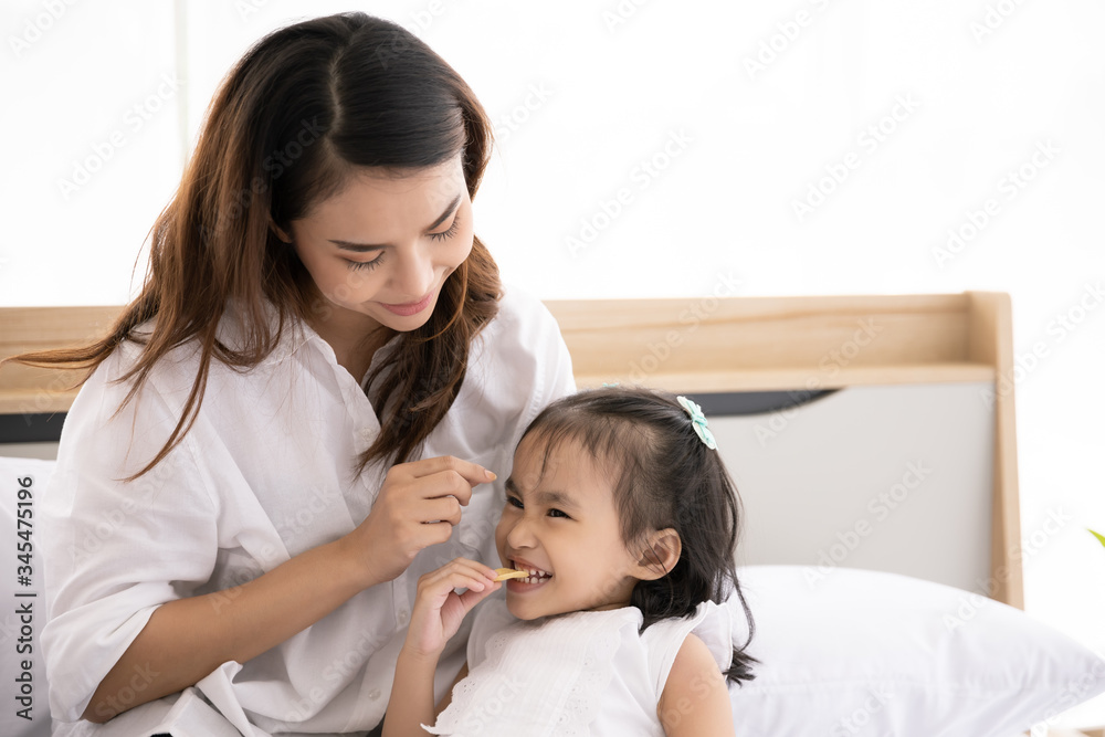 Happy Asian family. Single mother and Daughter aged three eat snacks on the bed in the house together Happy Asian family. Single mother and Daughter aged three eat snacks on the bed in the house together