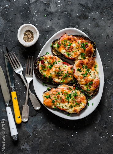 Baked eggplant with ham, tomatoes and mozzarella - delicious appetizer, tapas on a dark background, top view