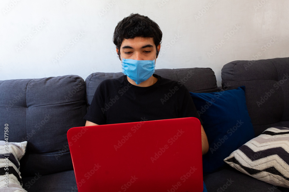 young man wearing a blue medical mask working from home on his laptop due to covid 19 quarantine young man wearing a blue medical mask working from home on his laptop due to covid 19 quarantine