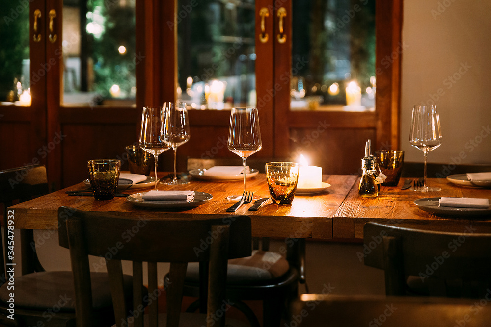 Crop image of romantic fine dining table with cutleries, plates, wine glasses, napkins and naperies on the table. Light source from candle light. Crop image of romantic fine dining table with cutleries, plates, wine glasses, napkins and naperies on the table. Light source from candle light.