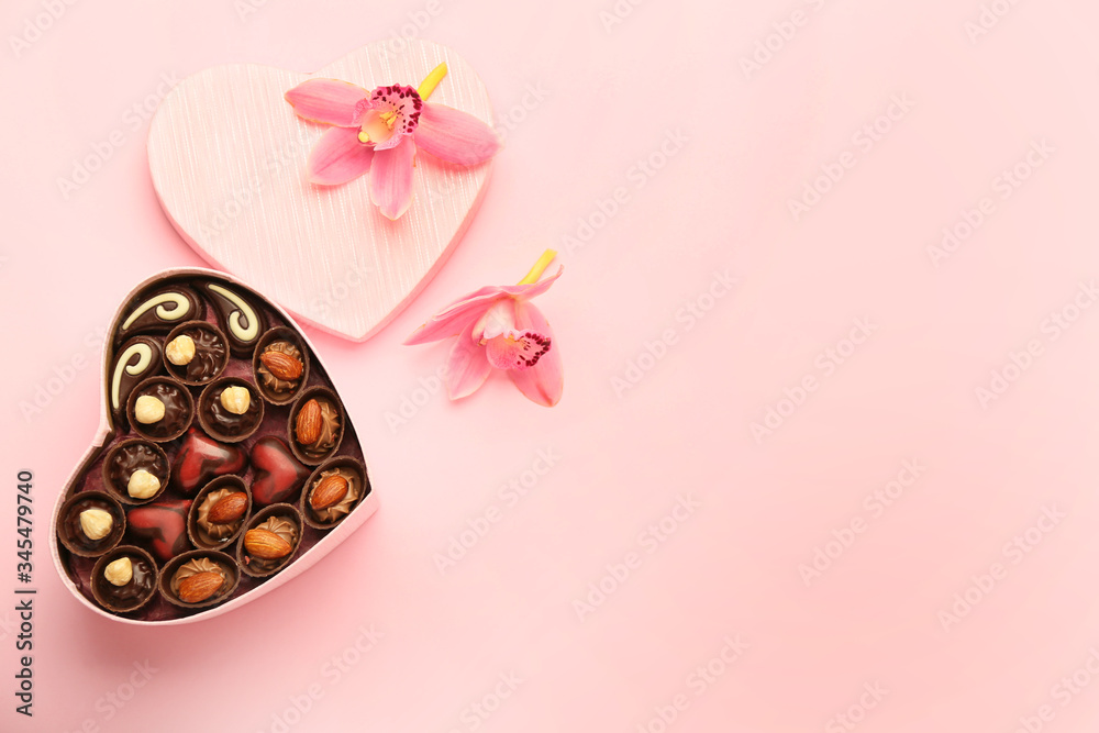 Heart-shaped box with chocolate candies on color background