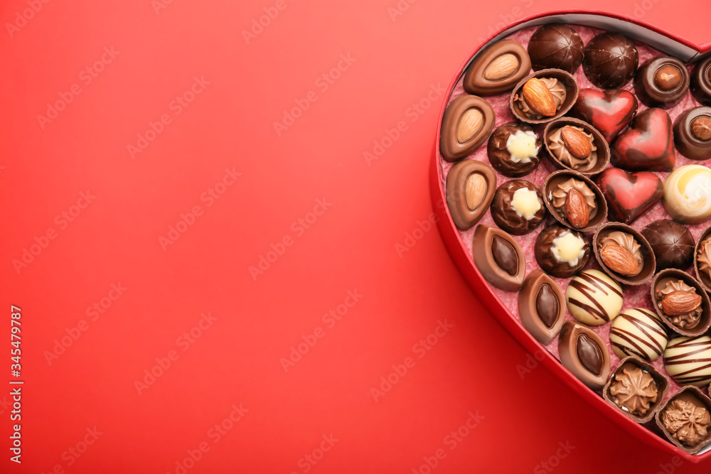 Heart-shaped box with chocolate candies on color background