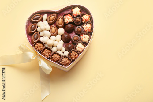 Heart-shaped box with chocolate candies on color background © Pixel-Shot
