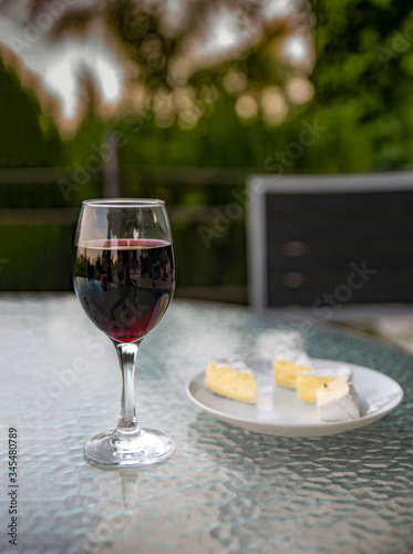 Glass of red wine, plate with cheese on a glass table. Vintage style.