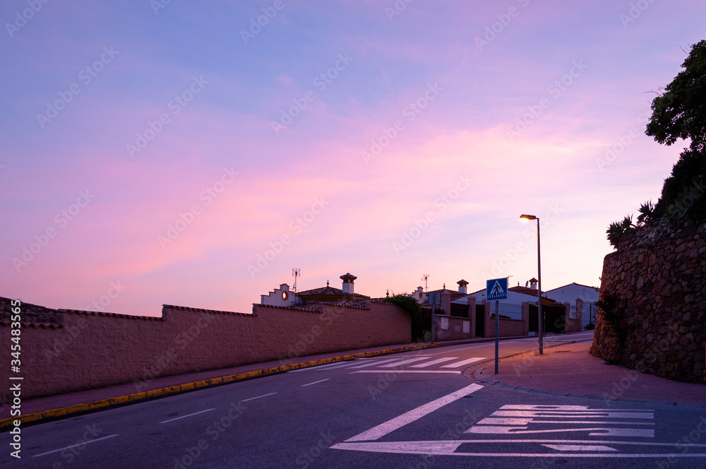 Street lamp illuminates a crosswalk at a crossroads against the sky during sunset
