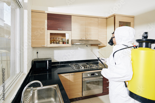 Cleaning service worker desinfecting all surfaces in kitchen with checmical spray