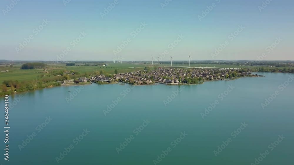 Aerial drone shot of panning to the left on the lake revealing the suburban and flat landscape with windmills in the Netherlands. Aerial drone shot of panning to the left on the lake revealing the suburban and flat landscape with windmills in the Netherlands.