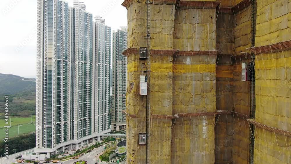 Traditional Bamboo Scaffolding covering a new Downtown Hong Kong residential skyscraper Building, climbing up with a small service elevator, Aerial view.