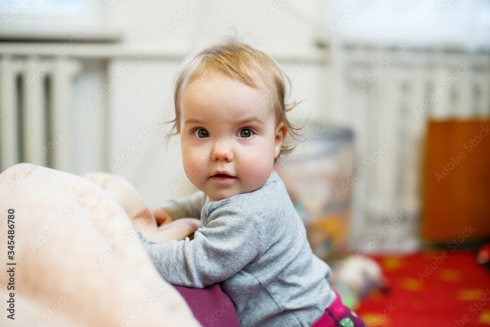 Photo portrait of a baby girl with pink cheeks. Baby gets to his feet