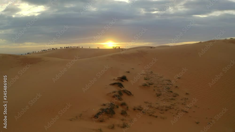 Rising aerial drone above red sand dune to reveal people on horizon at sunset Rising aerial drone above red sand dune to reveal people on horizon at sunset