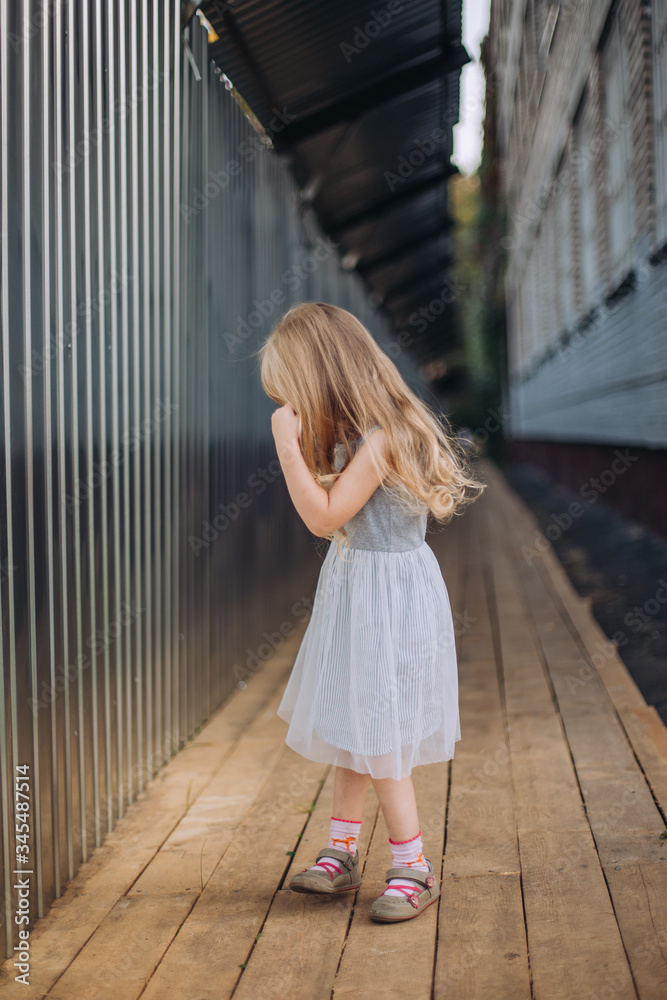 Little girl turning away from camera, standing alone in a tunnel, wearing grey dress and pink socks, blonde, long hair Little girl turning away from camera, standing alone in a tunnel, wearing grey dress and pink socks, blonde, long hair