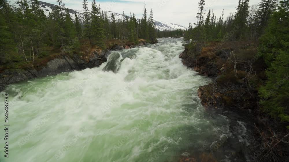 A wild mountain river in the Borgfjell national park. The torrent of turbid white water,  fed by melting snow, rushing down the riverbed, overflowing the banks.