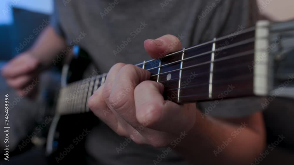 Man practices chords on electric guitar at home sitting on couch, side on view from guitar neck.