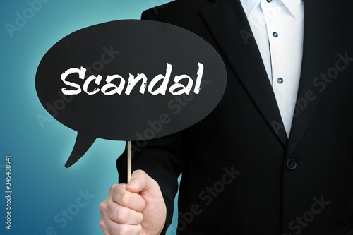Scandal. Lawyer in suit holds speech bubble at camera. The term Scandal is in the sign. Symbol for law, justice, judgement