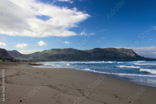 evocative image of sandy beach with rough sea headland in the background and clouds