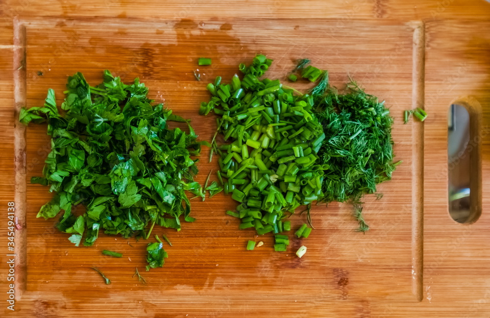 Sliced parsley, green onions and dill close-up on a wooden cutting Board in the kitchen Sliced parsley, green onions and dill close-up on a wooden cutting Board in the kitchen