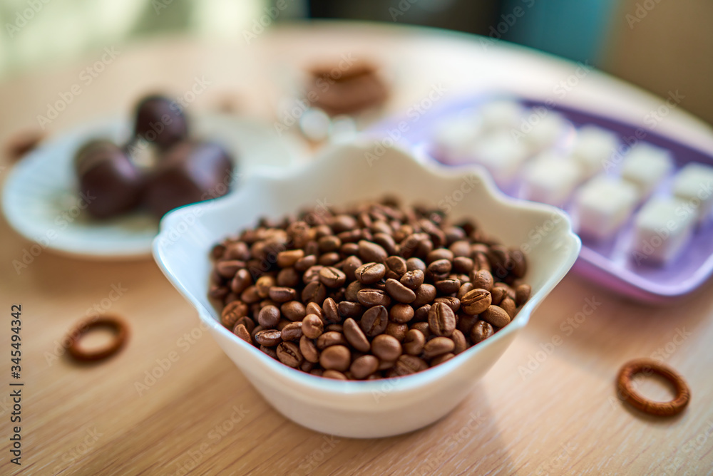 A white plate with a handful of coffee beans is standing on the table. Selective focus A white plate with a handful of coffee beans is standing on the table. Selective focus