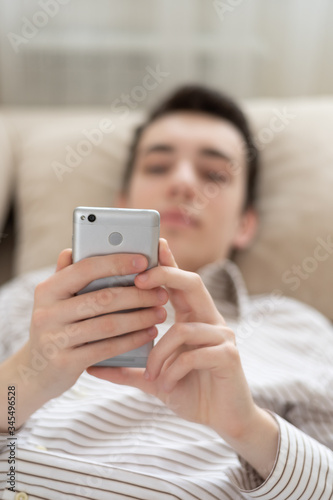 Teenager young man lying on sofa at home, holding and using smart phone