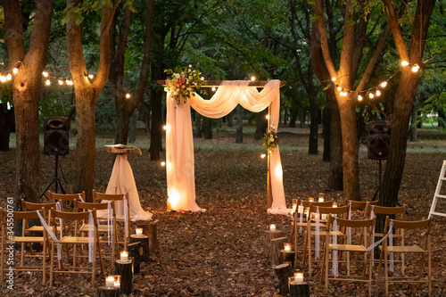 Wedding arch in the woods with light bulbs. Beautiful wedding rustic in the forest. Seats for guests at a beautiful wedding with light bulbs in the forest. Overall plan.
