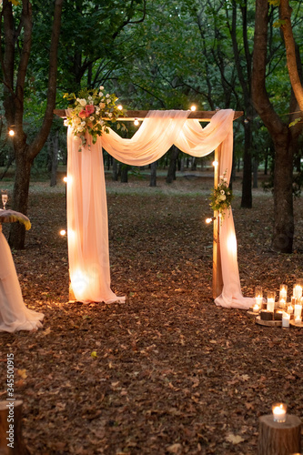 Wedding arch in the woods with light bulbs. Beautiful wedding rustic in the forest. Seats for guests at a beautiful wedding with light bulbs in the forest. Overall plan.