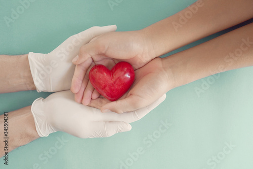 Doctor hands with medical gloves holding child hands and red heart, health insurance, donation, charity during covid-19 coronavirus pandemic, saving life, thank you and appreciation to doctor