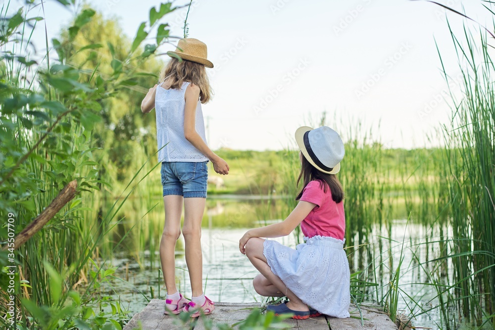 Girls children on wooden pier of lake in reeds, playing with water, talking
