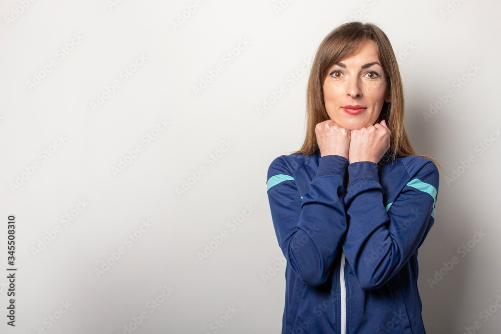 beautiful young woman in a 90s sports jacket, hands with her fists holds her chin on a light background. Trendy sport style concept beautiful young woman in a 90s sports jacket, hands with her fists holds her chin on a light background. Trendy sport style concept
