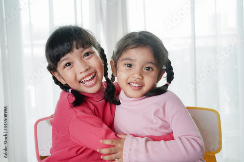 Happy Asian little child girl hugging and have fun with her happy sister or friend in the living room at home. family and childhood concept.