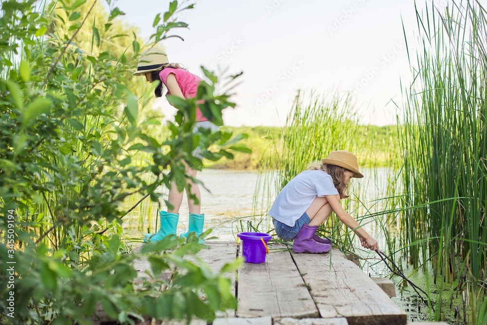 Children two girls together playing with water on lake on wooden pier in reeds Children two girls together playing with water on lake on wooden pier in reeds
