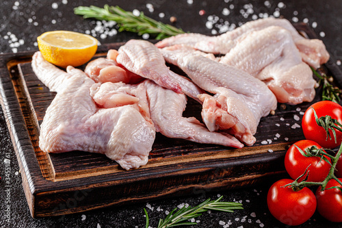 Raw meat. Chicken wings lie on a wooden board with vegetables and spices on a black background. background image, copy space text