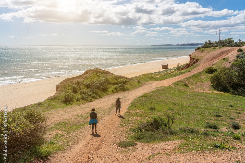 Two girls athletes in sports uniforms, walk along the cliff shore, in the summer near the sea. Beach of Falesia, Vilamoura Albufeira, Portugal.