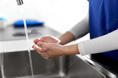 hygiene, health care and safety concept - close up of female doctor or nurse washing hands with soap and water at hospital