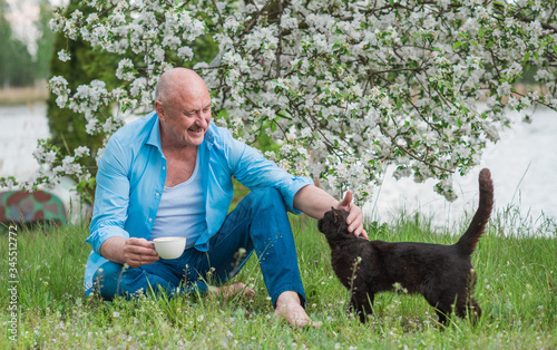 Portrait of Happy Mature man with a black cat at nature. Concept of senior lifestyle