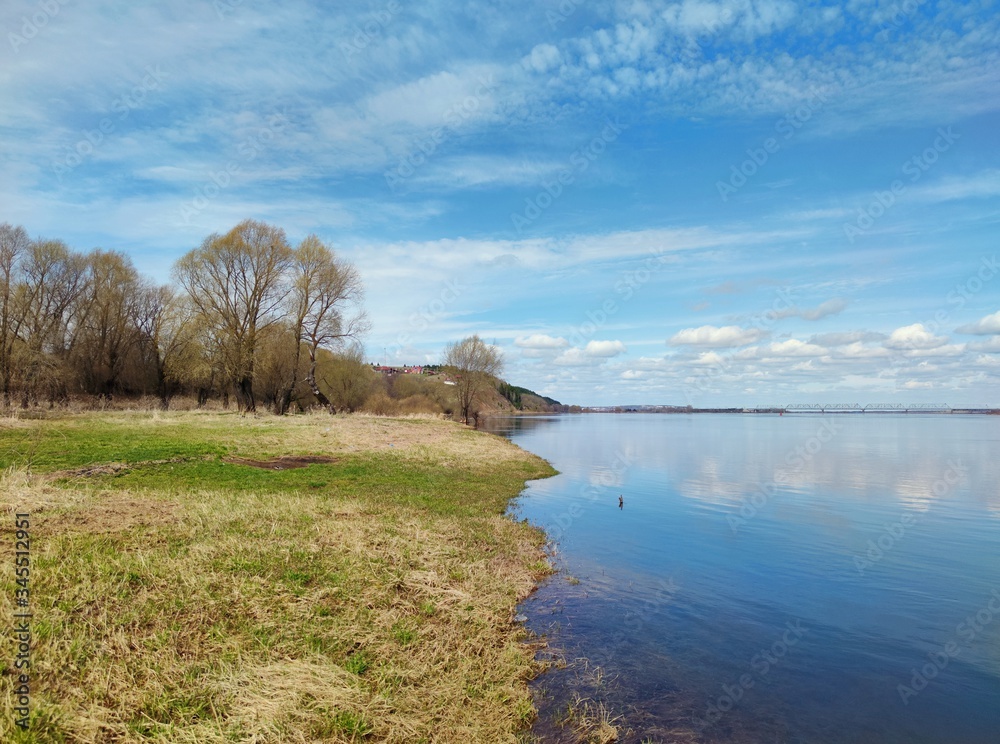 sunny landscape by the river against a beautiful blue sky with clouds