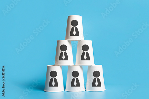 Pyramid-shaped paper cups on a blue background. Concept of corporation, friendly team, career ladder. Banner. Added icons in the form of a man. Copy space