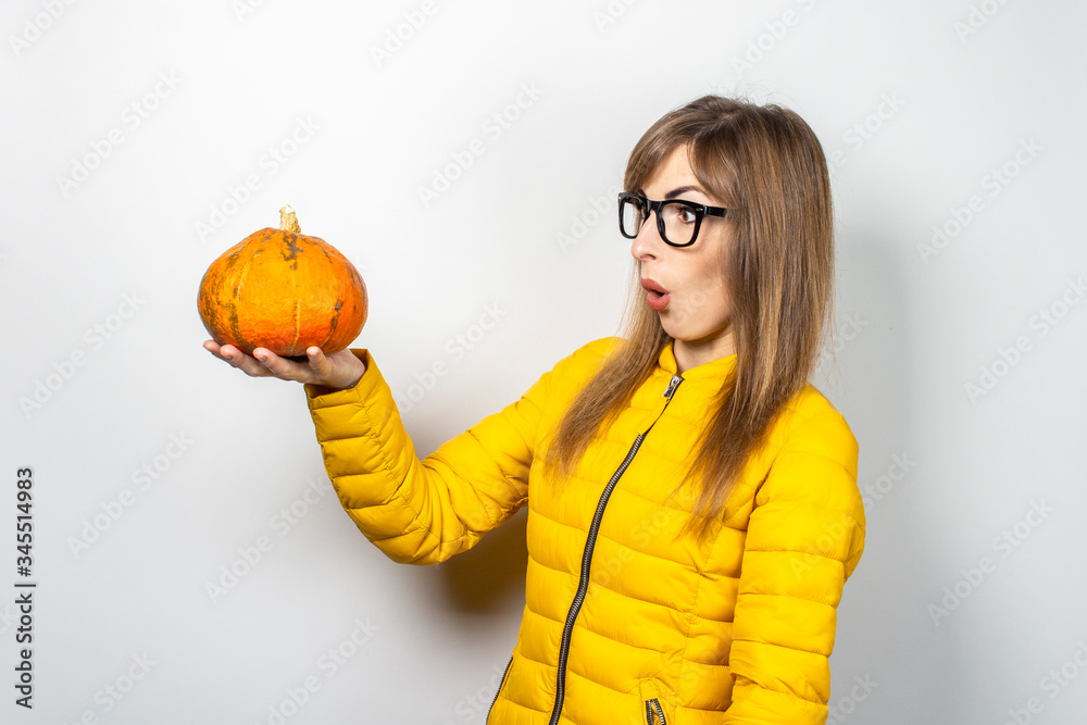 young girl in a yellow jacket holds a pumpkin with a frightened face on a light background. Halloween concept, autumn, celebration young girl in a yellow jacket holds a pumpkin with a frightened face on a light background. Halloween concept, autumn, celebration