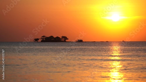 small island at horizon in tropical sea, late evening time, deep orange sky and low sun