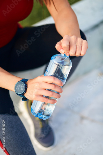 Thirsty young sporty woman making pause and drinking water during exerising. photo