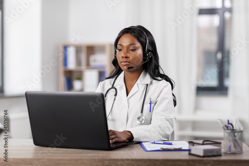 medicine, online service and healthcare concept - african american female doctor or nurse with headset and laptop having conference or video call at hospital