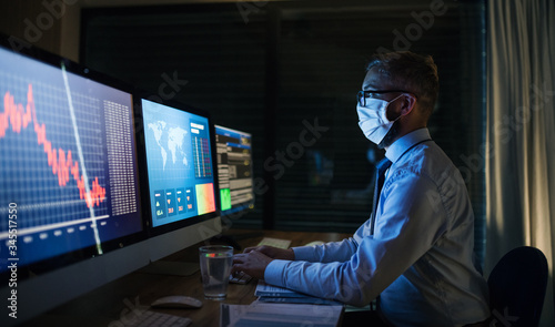 Businessman with computer sitting at desk, working late in office. Financial crisis concept.