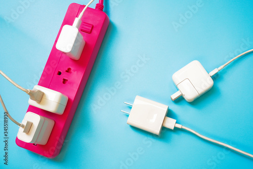 Pink extension power strip with only one socket left while there are 2 white mobile charger await to charge ,on blue pvc background ,strive for limited or shortage resource and competition concept 