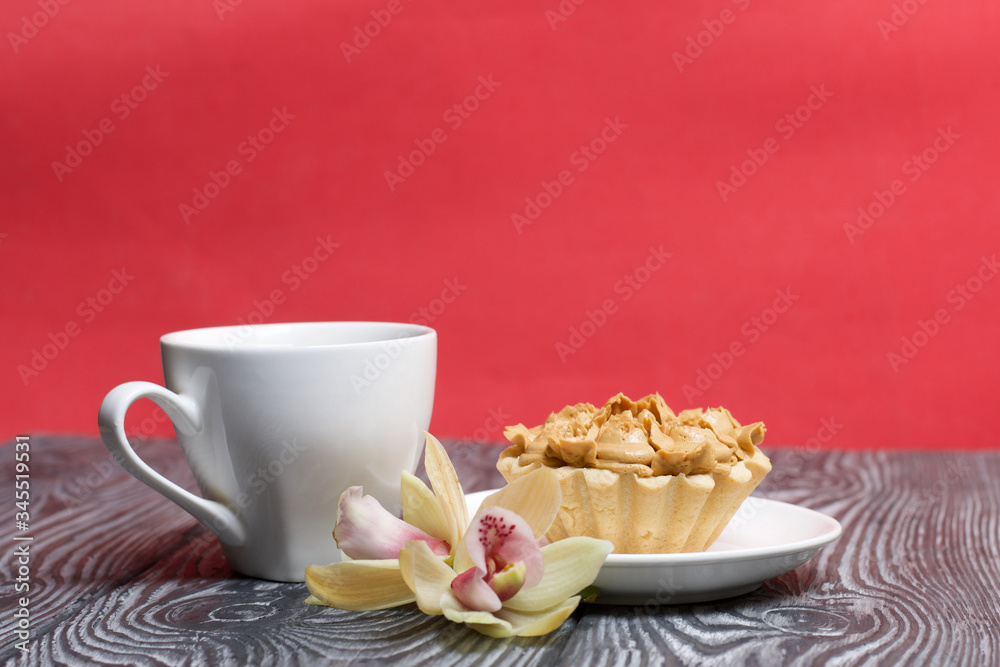Cupcake and a cup of coffee with milk. Nearby are orchid flowers. Cake decorated with flowers made of butter cream. The cream has a caramel color. On brushed pine boards painted black. Cupcake and a cup of coffee with milk. Nearby are orchid flowers. Cake decorated with flowers made of butter cream. The cream has a caramel color. On brushed pine boards painted black.
