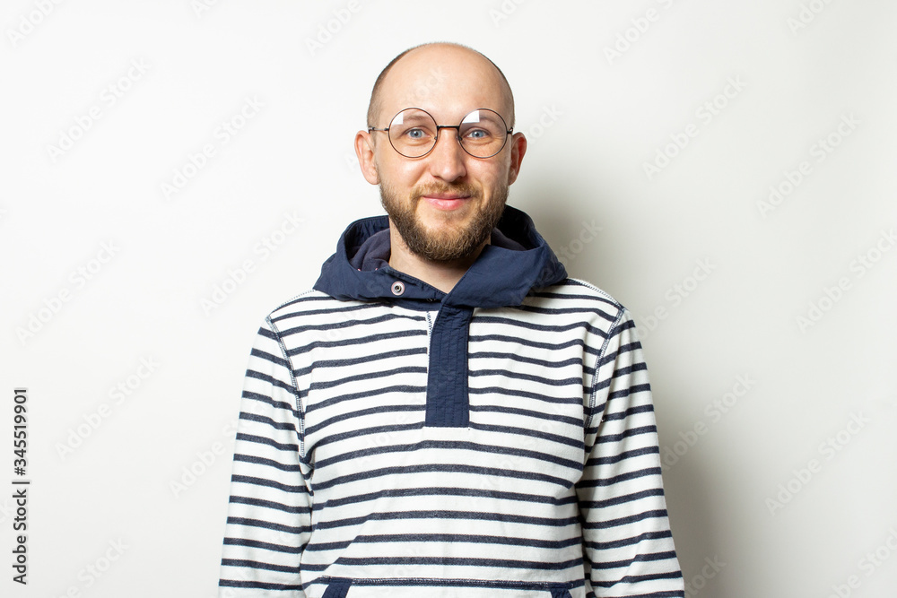 Portrait Young man with a beard in glasses a jacket with a hood on an isolated light background. Emotional face Portrait Young man with a beard in glasses a jacket with a hood on an isolated light background. Emotional face