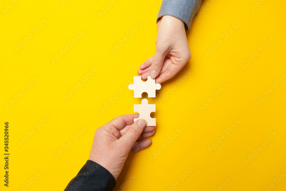Fototapeta premium Dwie ręce łączą puzzle na żółtym tle. Współpraca i praca zespołowa w biznesie. Współpraca zapewniająca sukces.