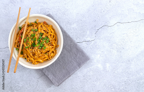 Chili noodles with bamboo chopsticks and linen napkin on the light background. Asian vegetarian meal. Top view, copy space