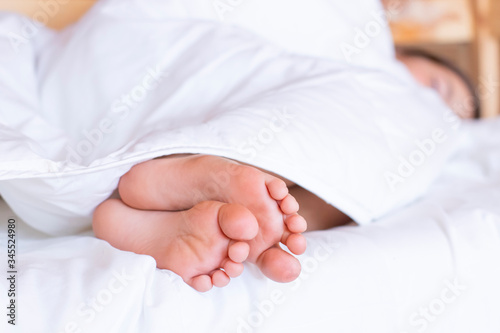 Child feet under the clear soft white blanket. Tenderness of morning dream