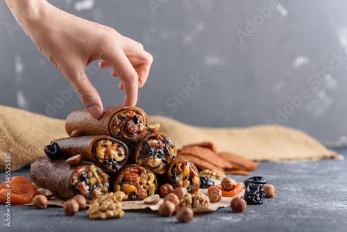 pyramid pastilles dried fruits, nuts, honey with hand on grey background, Eastern sweetness concept, fruit roll-up