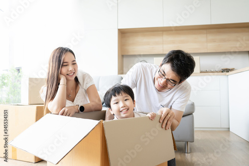 Asian family happy smile playing together during unpacking at new home, kids laughing sitting in card board box, playful in moving house day concept.