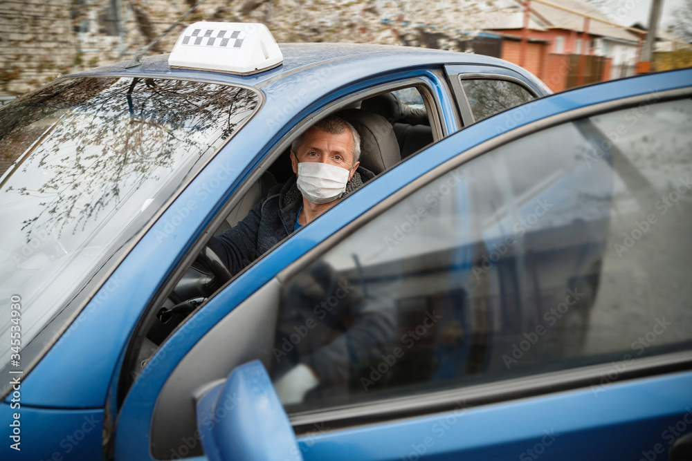 A man driving a car in a protective medical mask and gloves. Safe drive in a taxi during a pandemic coronavirus. Protect the driver and passengers from bacteria and virus infection in quarantine